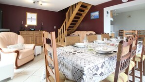 A dining area with a patterned tablecloth, wooden chairs, a staircase, and a clock on the wall.
