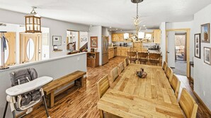 A spacious dining area with a long wooden table and benches, a kitchen with wooden cabinets, and a view of the outdoors.