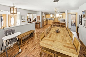 A spacious dining area with a long wooden table and benches, a kitchen with wooden cabinets, and a view of the outdoors.