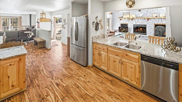 A modern kitchen with wooden cabinets, stainless steel appliances, a stone fireplace, and a dining area with a view.
