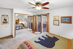 A bedroom with a bed, a ceiling fan, a large mirror, and a sliding glass door leading to a balcony.