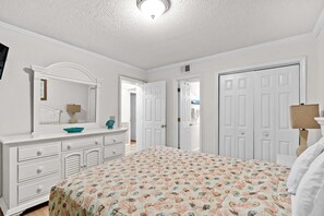 Un dormitorio con cama, cómoda, espejo y dos puertas.