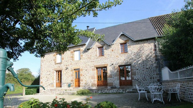A stone building with a sloped roof, multiple windows, and a small garden with flowers and chairs. - House near Mont Saint Michel - Semi-detached in Lolif (Lolif)