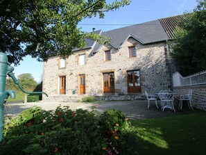 Un bâtiment en pierre doté d’un toit en pente, de nombreuses fenêtres et d’un petit jardin agrémenté de fleurs et de chaises.
