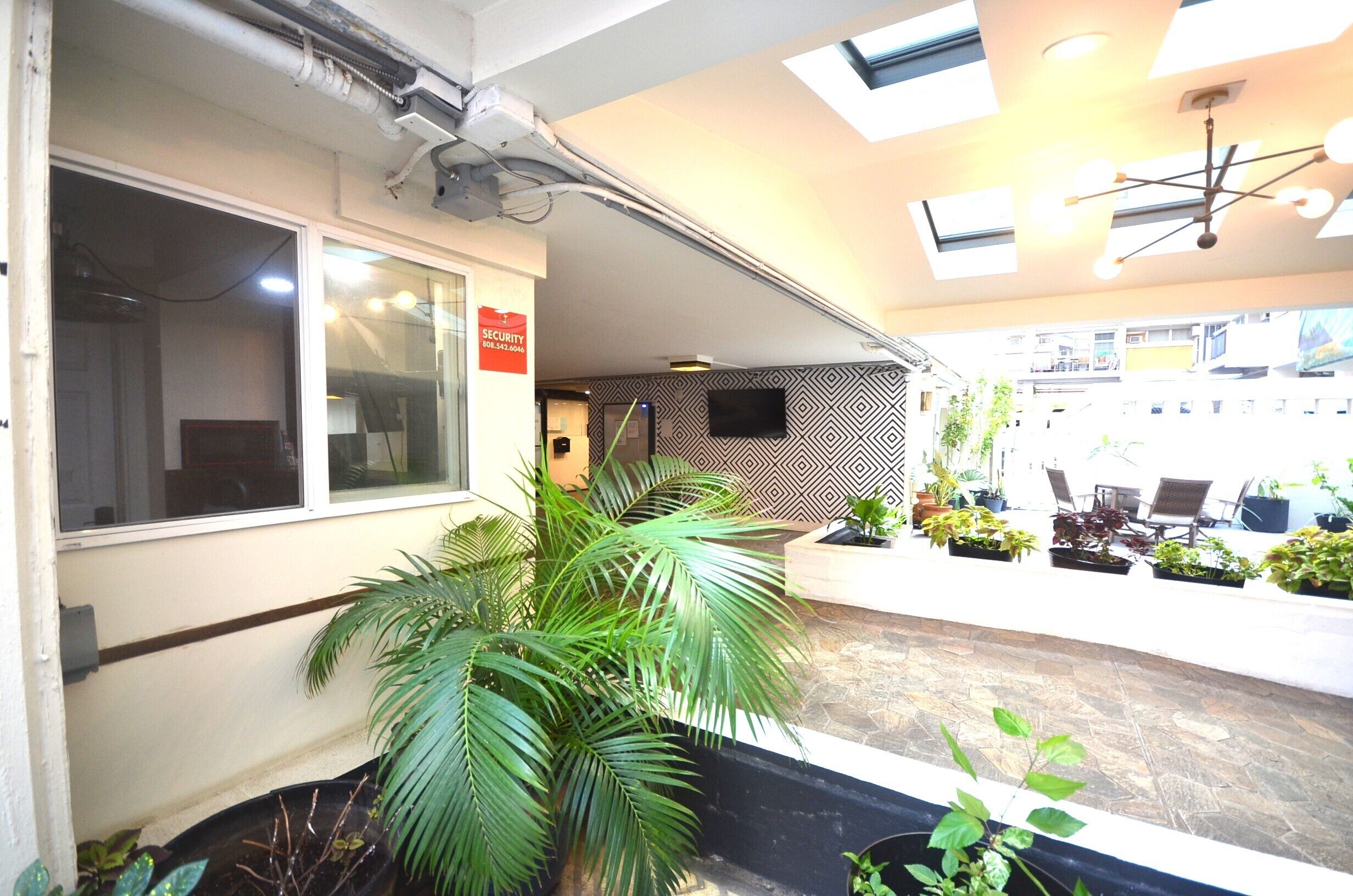 A reception area with a security sign, potted plants, and a patterned wall.