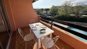 Un balcon avec une table dressée pour deux personnes, des chaises et une vue sur une piscine et la verdure.