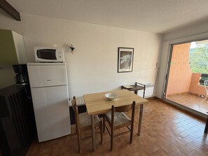 Uma cozinha compacta com micro-ondas, geladeira, mesa de jantar com cadeiras e uma pequena janela.