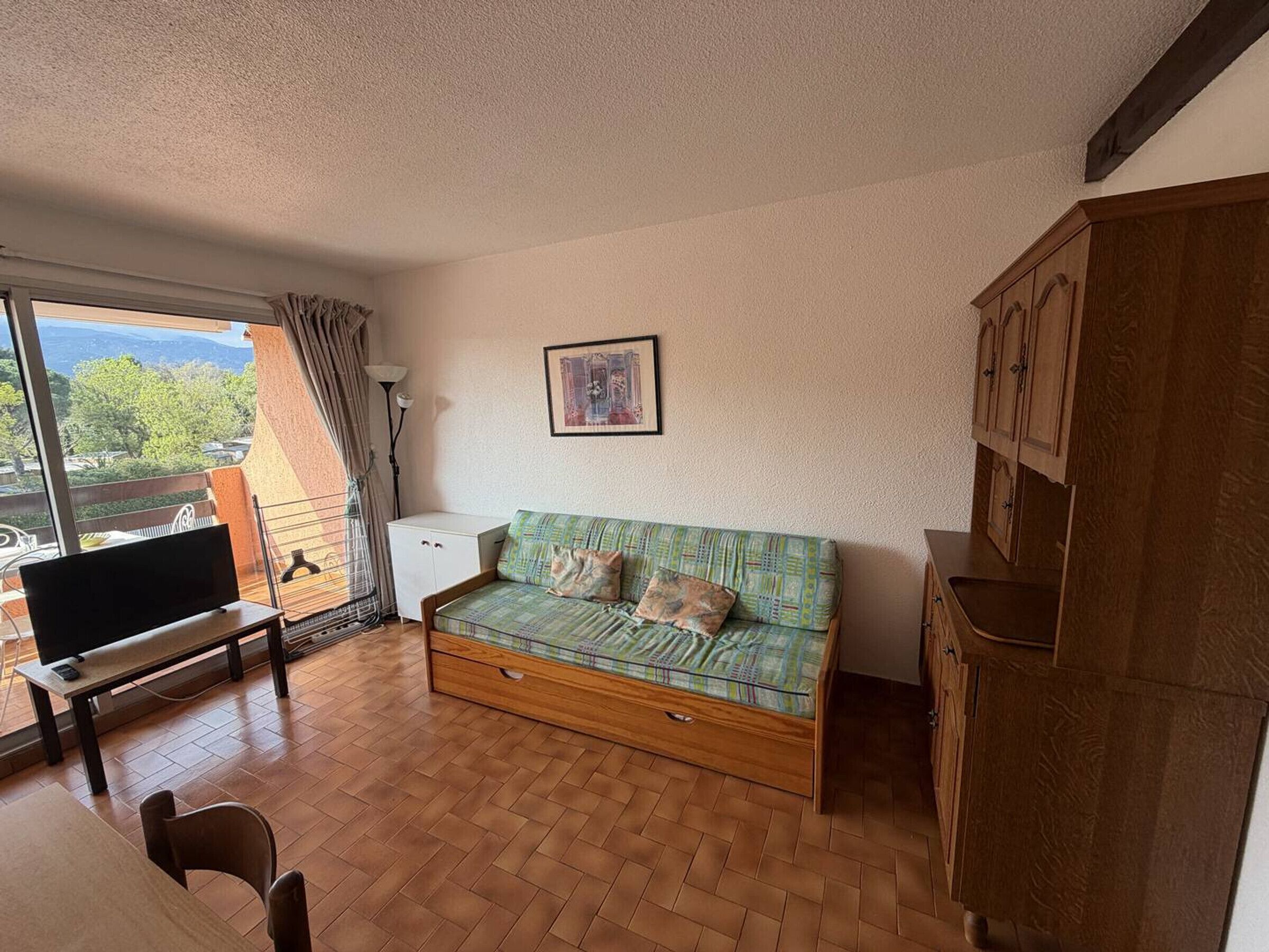 A cozy room with a sofa, a TV, a dining table, and a view of the outdoors.