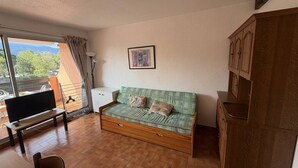 Une pièce confortable avec un canapé, une télévision, une table à manger et une vue sur l’extérieur.