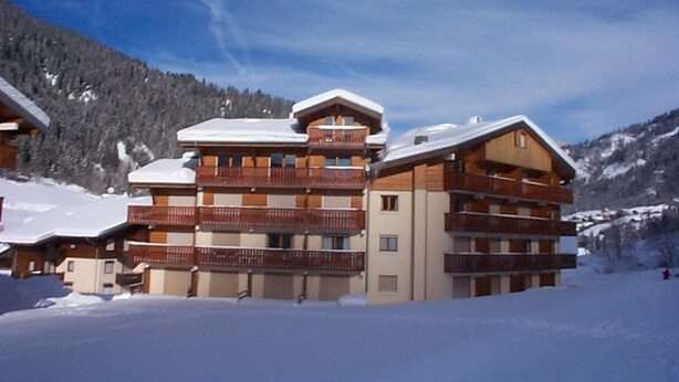 A multi-story hotel with balconies, set against a snowy mountain backdrop. - Cozy apartment with terrace for 4 people and parking in Châtel (Châtel)