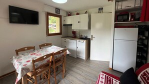 A compact kitchen with white cabinets, a microwave, and a refrigerator. There's a dining table with chairs and a TV mounted on the wall. - Cozy apartment with terrace for 4 people and parking in Châtel (Châtel)