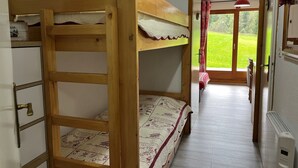 A bunk bed room with a wooden frame, a patterned bedspread, and a view of a green landscape through a door. - Cozy apartment with terrace for 4 people and parking in Châtel (Châtel)