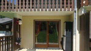 A covered patio area with a sliding glass door, a metal grill, and a trash bin. - Cozy apartment with terrace for 4 people and parking in Châtel (Châtel)