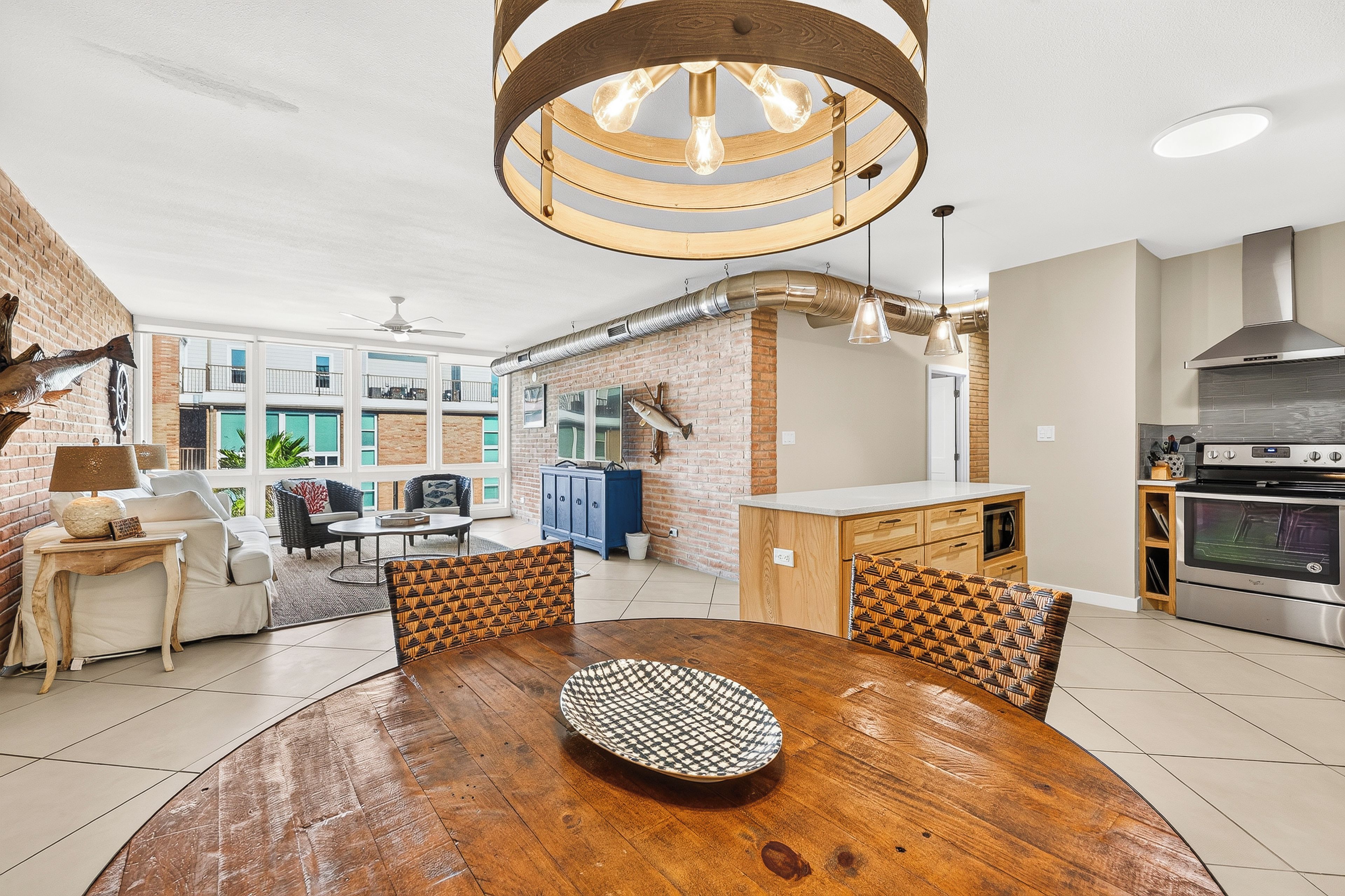 A modern kitchen with a built-in oven, a dining area with a wooden table and patterned chairs, and a brick wall with decorative fish.