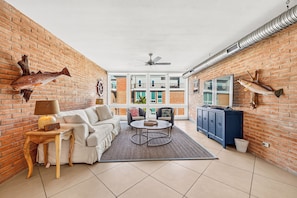 A spacious living area with a brick wall, a ceiling fan, a sofa, a coffee table, and a view of the outside. - This fabulous upscale condo is located right on the ship channel and in the hear (Port Aransas)