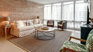 A living room with a brick wall, a sofa, two armchairs, a coffee table, and a TV on a stand. - This fabulous upscale condo is located right on the ship channel and in the hear (Port Aransas)