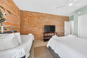 Een hotelkamer met twee bedden, een bakstenen muur, een flatscreen televisie en een plafondventilator.