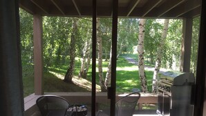 Eine überdachte Veranda mit zwei Stühlen, einem Grill und Blick ins bewaldete Gebiet.