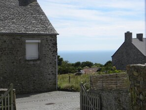 A stone building with a view of the sea, a paved pathway, and a wooden gate.