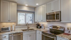 Una cocina con armarios blancos, un microondas de acero inoxidable, un tostador, una cafetera y un lavavajillas.