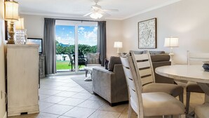 A modern living room with a grey sofa, a dining table with chairs, and a ceiling fan. - Fun, Easy & Sunset Views! Ground Floor Getaway – Islander 117 (Destin)