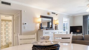 A dining area with a round table, chairs, a decorative centerpiece, a television, and a sofa in the background. - Fun, Easy & Sunset Views! Ground Floor Getaway – Islander 117 (Destin)