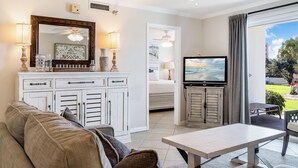A living room with a sofa, a coffee table, a TV, and a view of the outdoors. - Fun, Easy & Sunset Views! Ground Floor Getaway – Islander 117 (Destin)