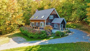 A wooden cabin with a sloped roof, a porch, and a gravel driveway. - Ayers Farm Cottage: 4 br, wood fireplace, a/c, deck, mountain view! (Stowe)