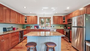 Une cuisine dotée de meubles en bois, d’un plan de travail en granit, d’appareils électroménagers en acier inoxydable et d’un îlot central avec des tabourets.