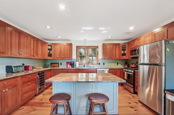 A kitchen with wooden cabinets, a granite countertop, stainless steel appliances, and a central island with stools. - Ayers Farm Cottage: 4 br, wood fireplace, a/c, deck, mountain view! (Stowe)