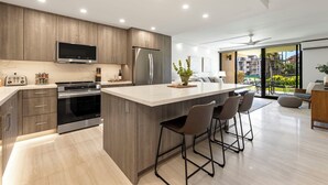 A modern kitchen with a central island, stainless steel appliances, and a large window offering a view of the outdoors.