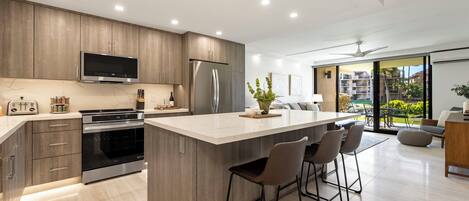 A modern kitchen with a central island, stainless steel appliances, and a large window offering a view of the outdoors.