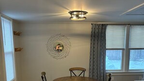 Un comedor con una mesa redonda y sillas, una lámpara fijada a la pared y un espejo decorativo.