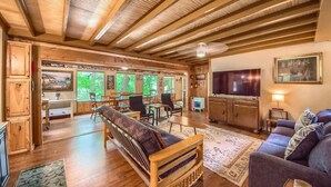 A spacious living area with a wooden ceiling, a sofa, a television, and a dining area with chairs and a table. - PRD 888 Ponderosa Cabin (New Braunfels)