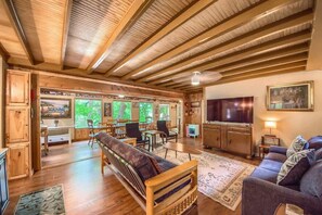 A spacious living area with a wooden ceiling, a sofa, a television, and a dining area with chairs and a table.