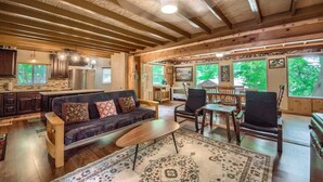 A spacious living area with a wooden ceiling, a sofa, chairs, a coffee table, and a rug. - PRD 888 Ponderosa Cabin (New Braunfels)