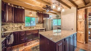 A kitchen with dark wooden cabinets, a granite countertop island, and a ceiling fan. - PRD 888 Ponderosa Cabin (New Braunfels)