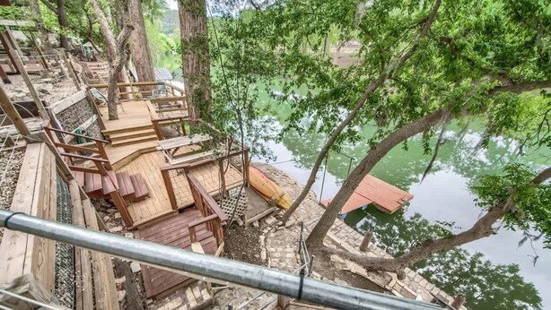 A wooden deck with a metal railing overlooking a body of water, surrounded by trees. - PRD 888 Ponderosa Cabin (New Braunfels)