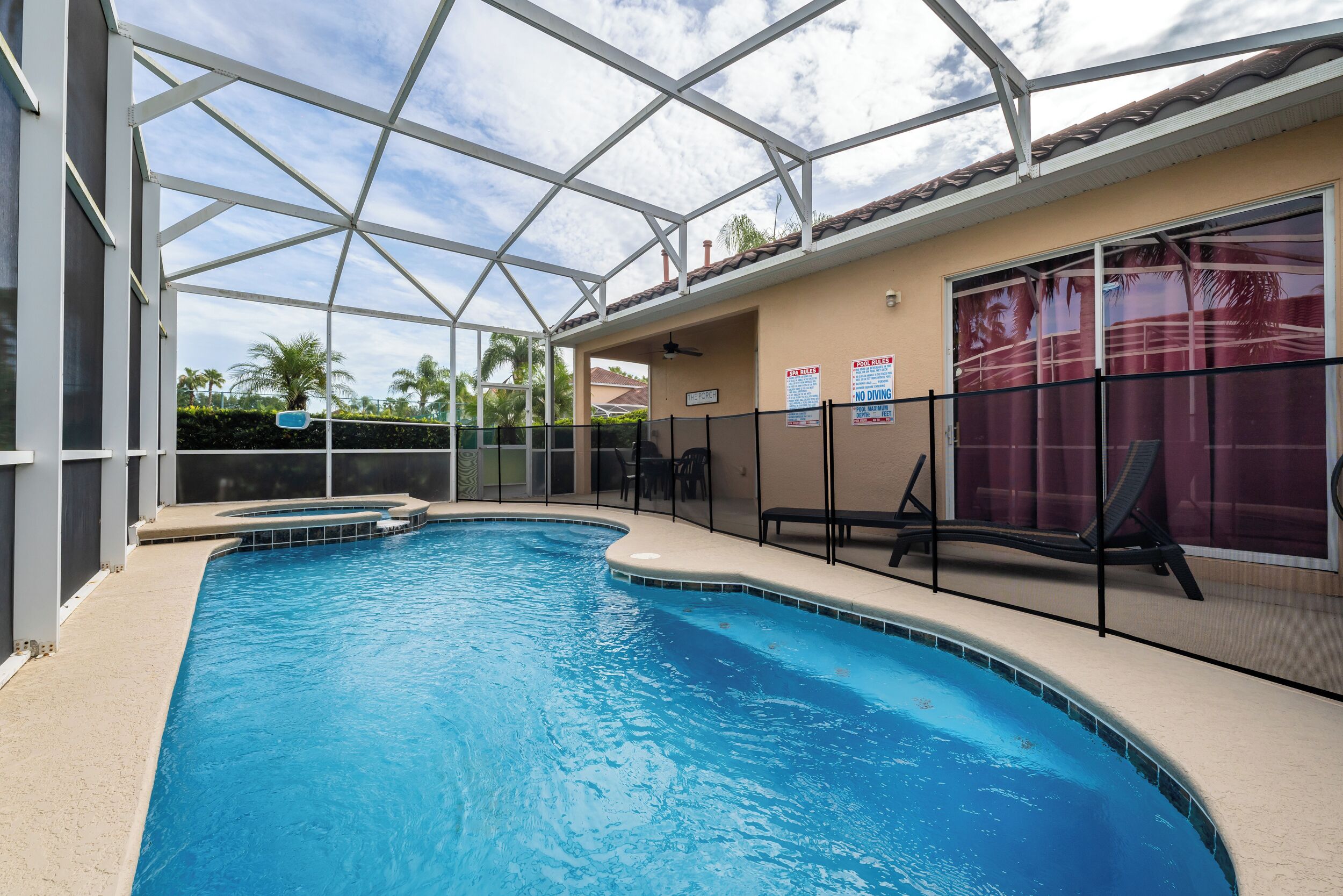 An indoor swimming pool with a glass ceiling, poolside chairs, and a view of palm trees.