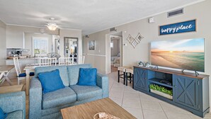 Ein Wohnzimmer mit blauem Sofa, einem Couchtisch und einem Fernseher auf einem Holzständer.