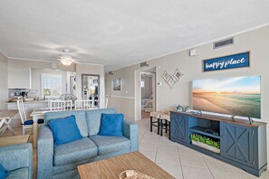 Sala de estar com um sofá azul, uma mesa de centro e uma TV sobre um suporte de madeira.
