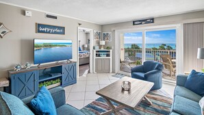 Ein Wohnzimmer mit Fernseher, blauen Sofas, einem Couchtisch und einem Balkon mit Meerblick.