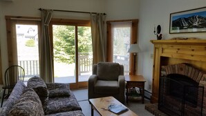 A living room with a sofa, armchair, and a fireplace. There is a window with blinds and a door leading outside. - Ski in/out 4 BR townhome directly on Raccoon Run and the Village Chair Lift !! (Jay)