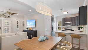 A modern kitchen with white cabinetry, a wooden dining table, and wicker bar stools. - New Owners of Dock Knocker! Brand New Look In Time For Spring Break 2025! (Pensacola)