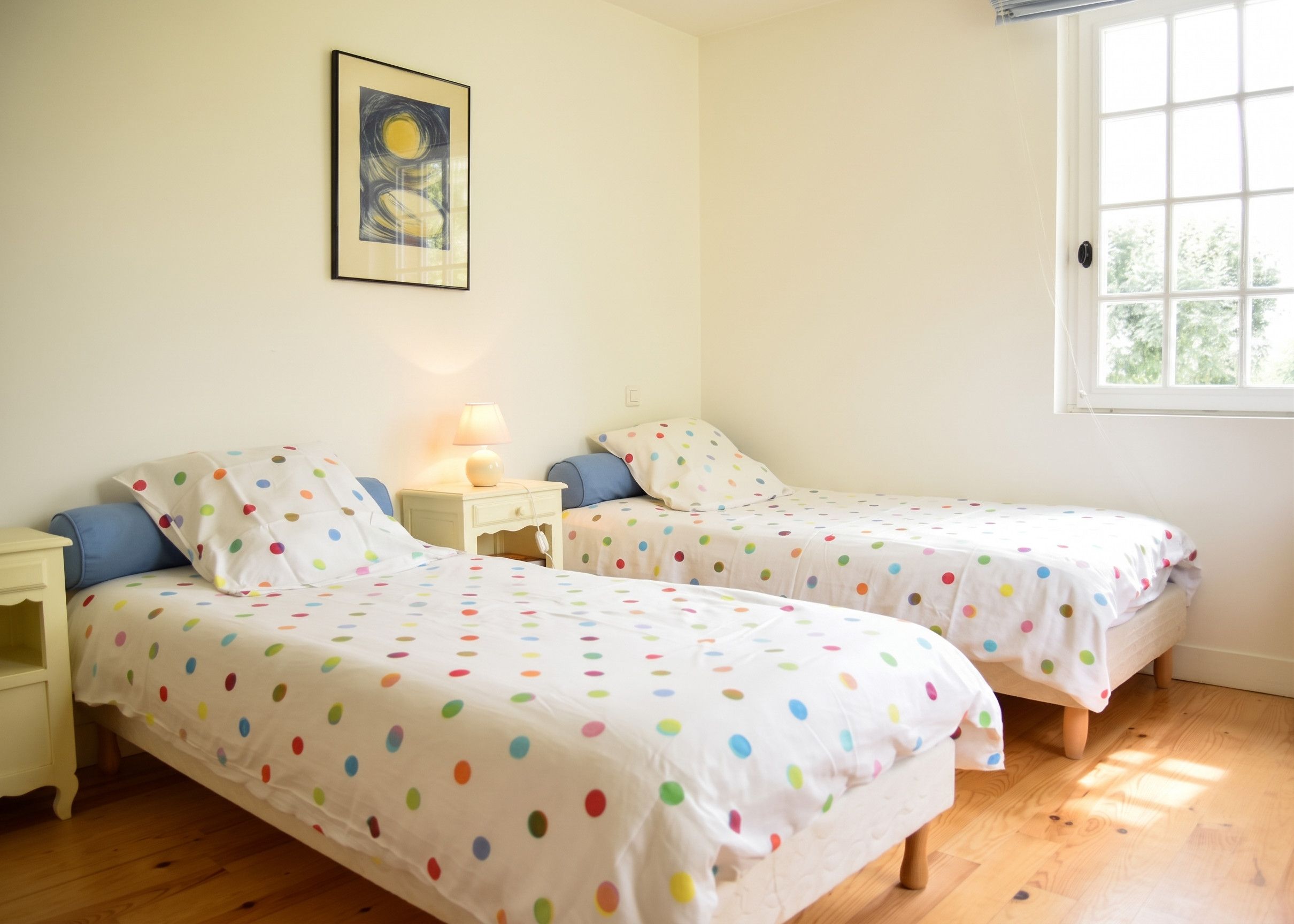 Een slaapkamer met twee eenpersoonsbedden, een nachtkastje met een lamp, een raam met zonwering en een ingelijst schilderij aan de muur.