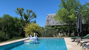 Una piscina con solárium de baldosas, sillas de descanso y una estructura de techo de paja.