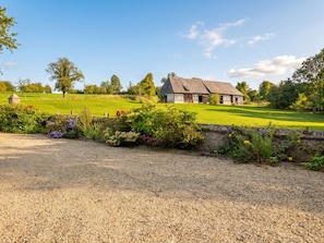 A rural property with a thatched-roof barn, a gravel driveway, and a well-maintained lawn.