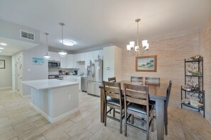 A modern kitchen with white cabinets, stainless steel appliances, a central island, and a dining area with wooden chairs and a chandelier. - Experience upscale coastal living in this fabulous condo with elevator access, p (Port Aransas)
