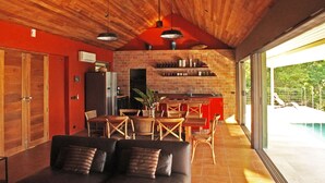 Un salón moderno con chimenea de ladrillo, techo de madera y ventanas amplias con vistas a una piscina.