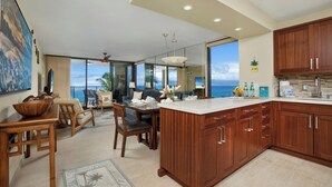A modern kitchen with wooden cabinets, a dining area with a view, and a large island. - Mahana Villas | Oceanfront 2 BR | Whale Watching | Car Incl. w/ 6+ Nights | MAH-611 by KBM (Lahaina)